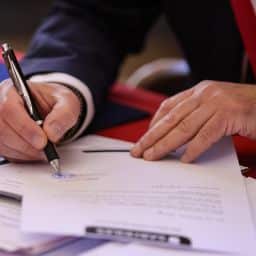 A person signs a document with a pen.