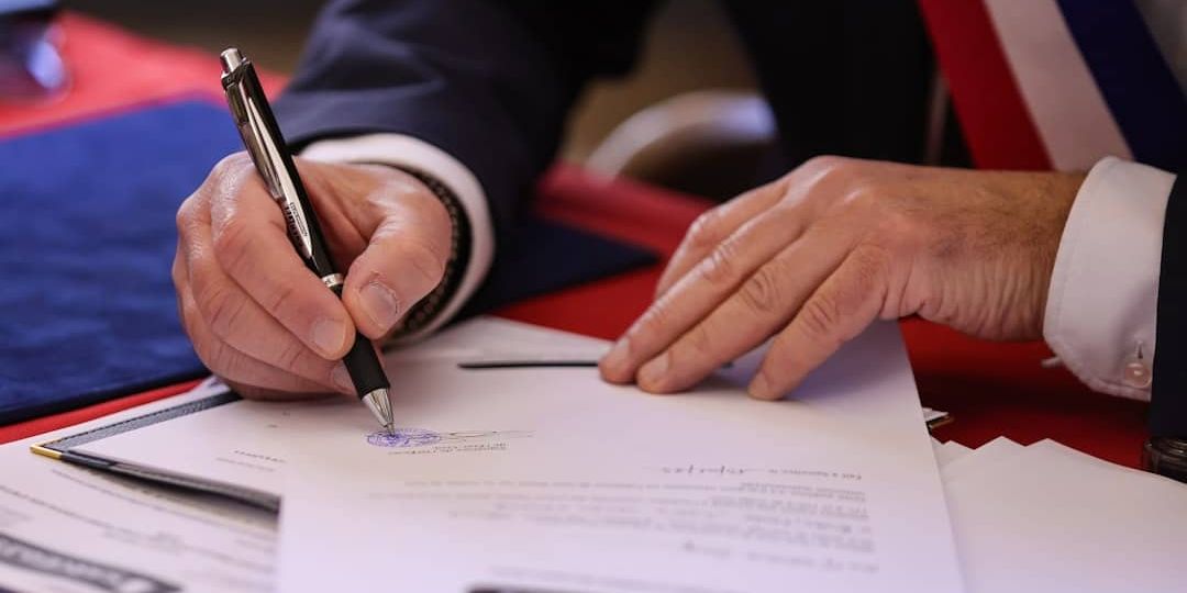 A person signs a document with a pen.