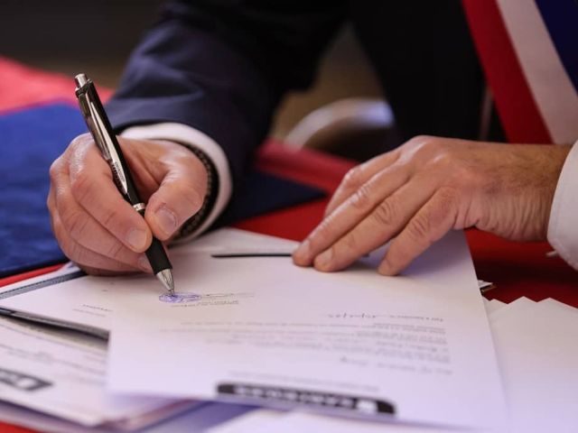 A person signs a document with a pen.